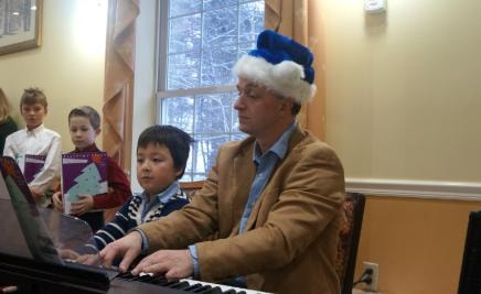Teacher playing piano with students during a holiday performance
